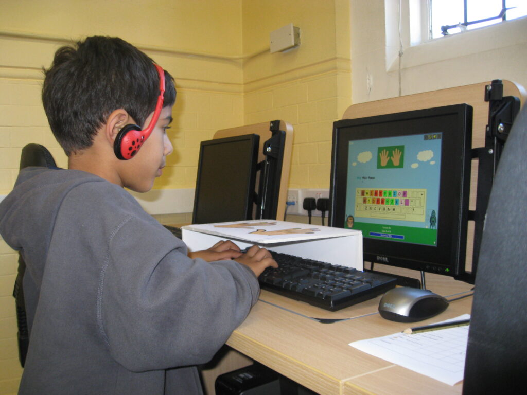 Child learning to touch type on a laptop with tutor support
